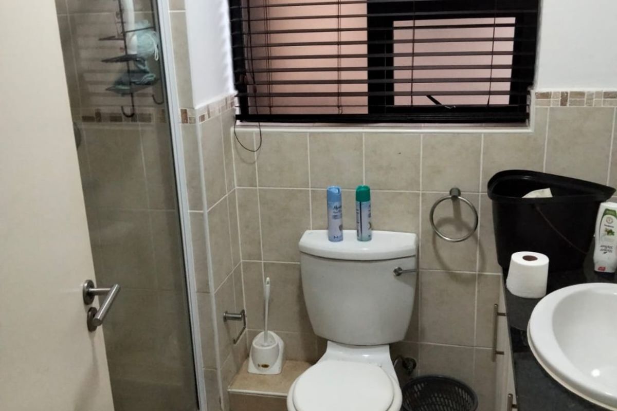 A functional bathroom featuring a shower enclosure, toilet, and vanity basin with tiled finishes and a window providing natural light.