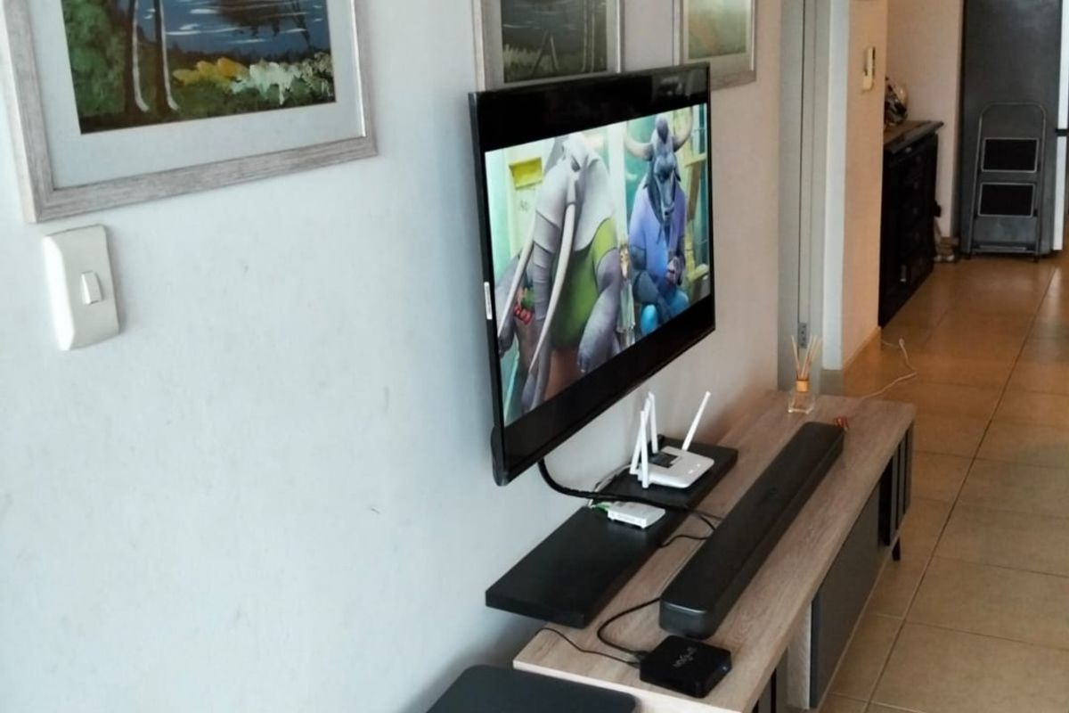 A living area featuring tiled flooring and a wall-mounted television setup, providing a functional space for entertainment.