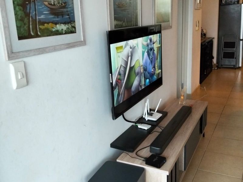 A living area featuring tiled flooring and a wall-mounted television setup, providing a functional space for entertainment.