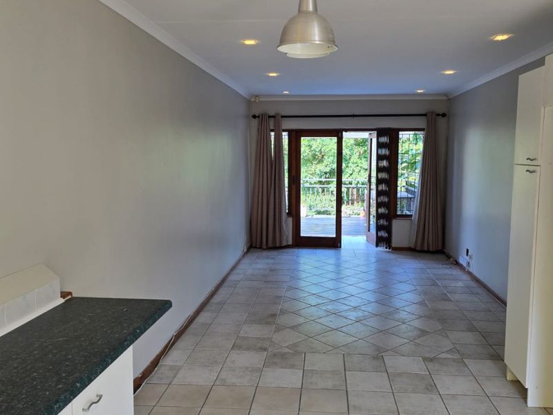 An open-plan living area featuring tiled floors, built-in cabinetry, and direct access to an outdoor balcony through double glass doors.