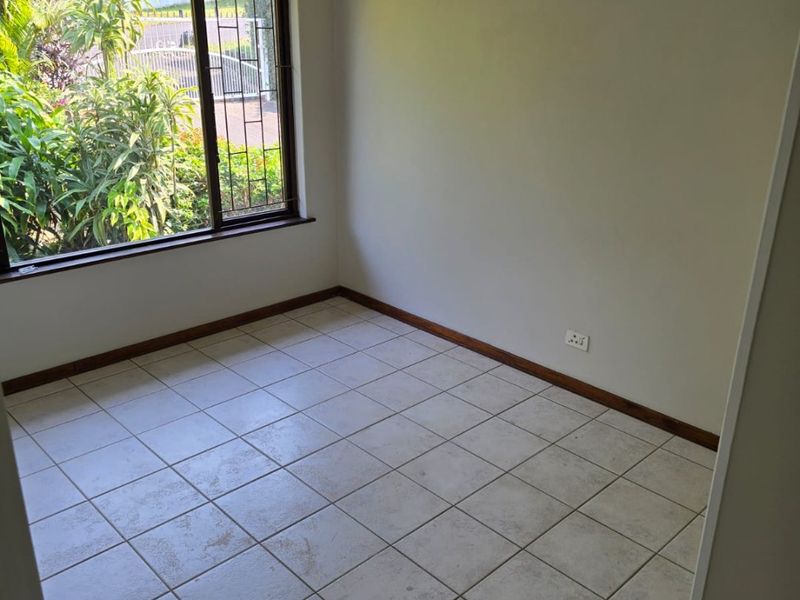 An empty bedroom featuring tiled flooring, a ceiling fan, and a window with security bars, offering a blank canvas for personalization.