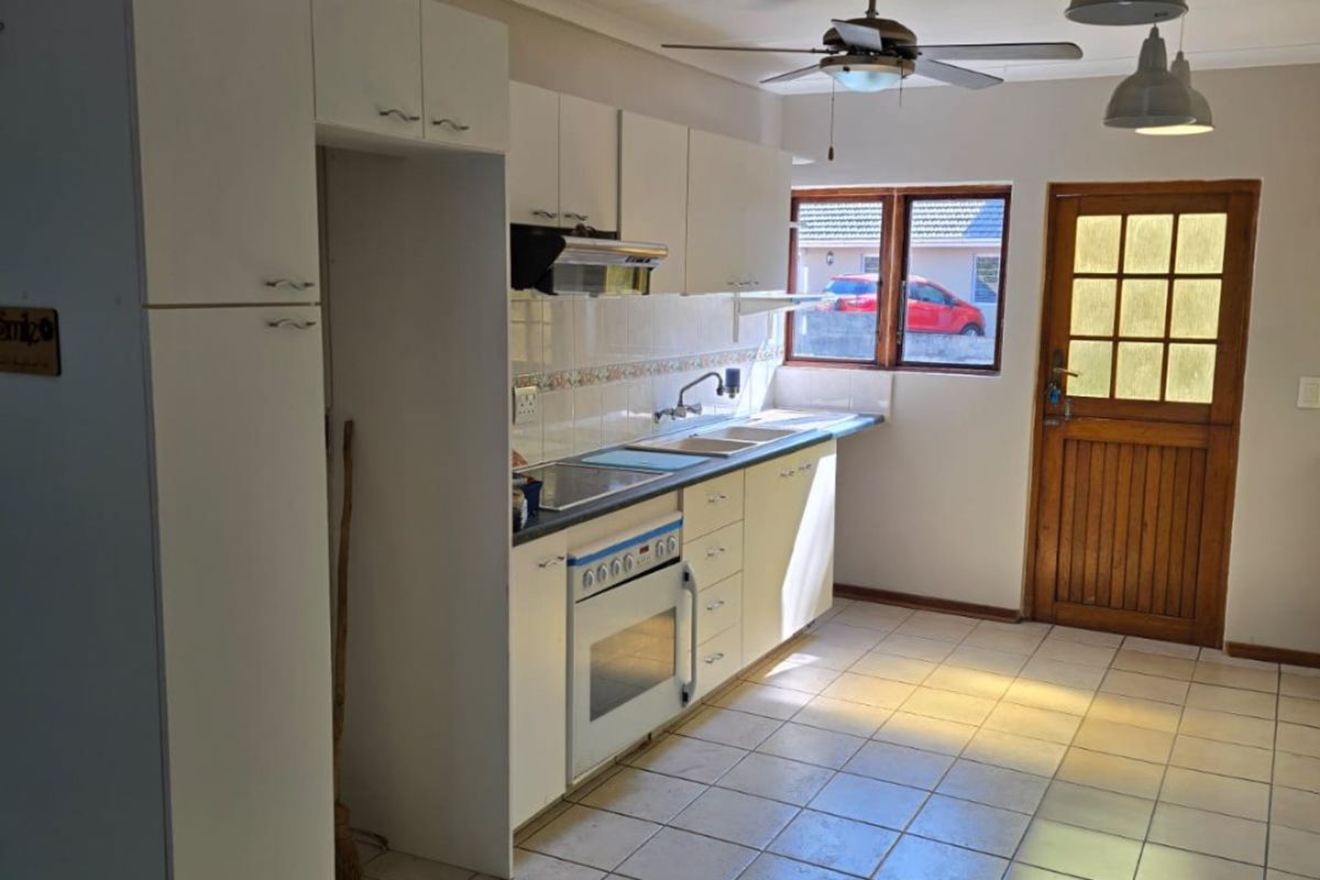 A functional kitchen featuring white built-in cabinetry, an integrated oven and hob, tiled flooring, and direct access to the exterior via a timber door.
