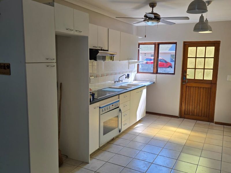 A functional kitchen featuring white built-in cabinetry, an integrated oven and hob, tiled flooring, and direct access to the exterior via a timber door.