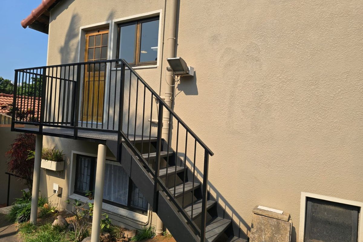 Exterior view of the property featuring a metal staircase leading to an upper-level balcony with a timber door and window access.