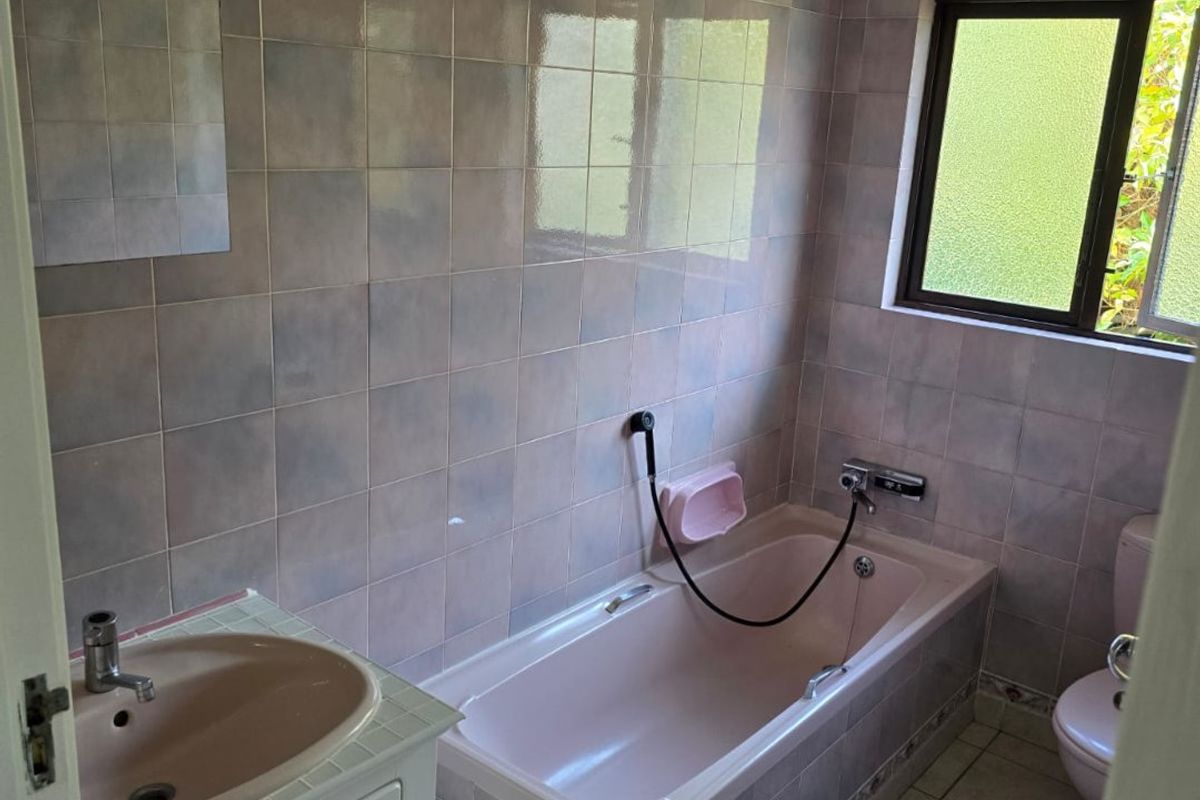 A dated bathroom featuring a built-in bathtub, vanity cabinet with basin, and toilet, finished with full-height wall tiling and floor tiles.