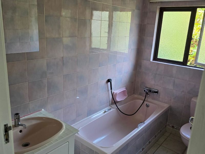 A dated bathroom featuring a built-in bathtub, vanity cabinet with basin, and toilet, finished with full-height wall tiling and floor tiles.