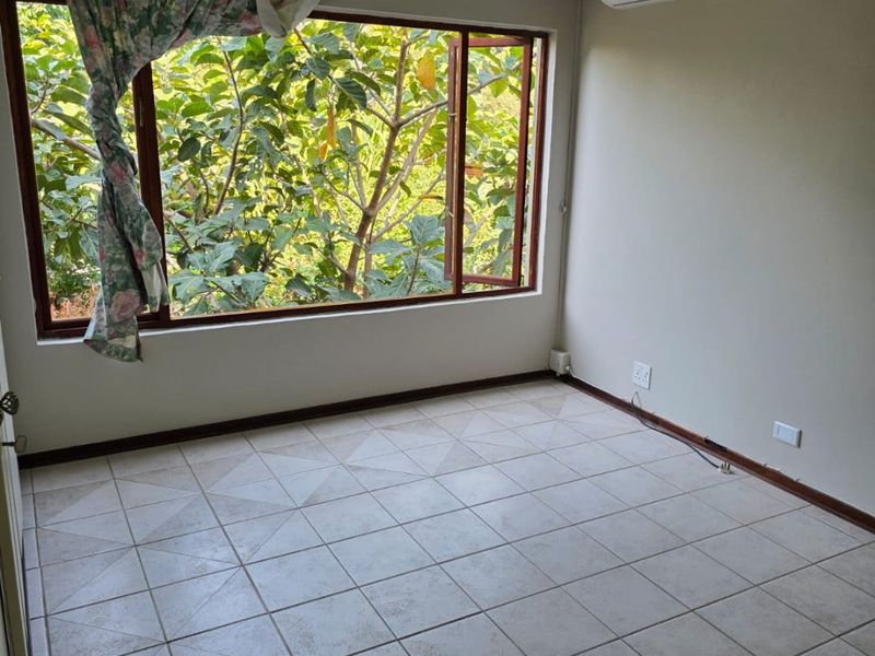 An empty bedroom featuring tiled flooring, recessed lighting, and a wall-mounted air conditioning unit with large windows overlooking greenery.
