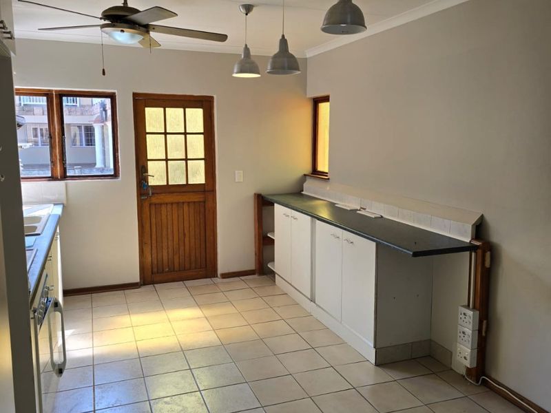 A functional kitchen space featuring tiled flooring, built-in cabinetry with dark countertops, pendant lighting, and a ceiling fan, with direct access to the exterior.
