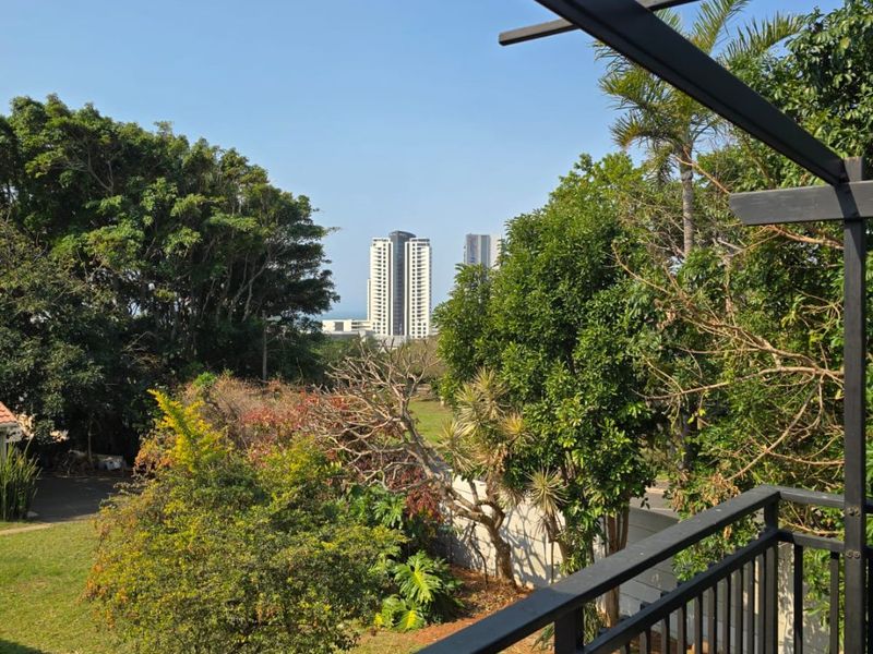A balcony featuring timber decking and a black metal railing, offering an elevated view of the surrounding trees and distant city skyline.