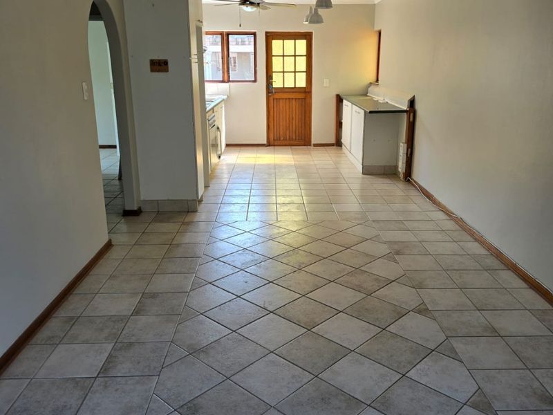 An open-plan living and kitchen area featuring tiled flooring, recessed lighting, a ceiling fan, and a timber-framed exterior door.