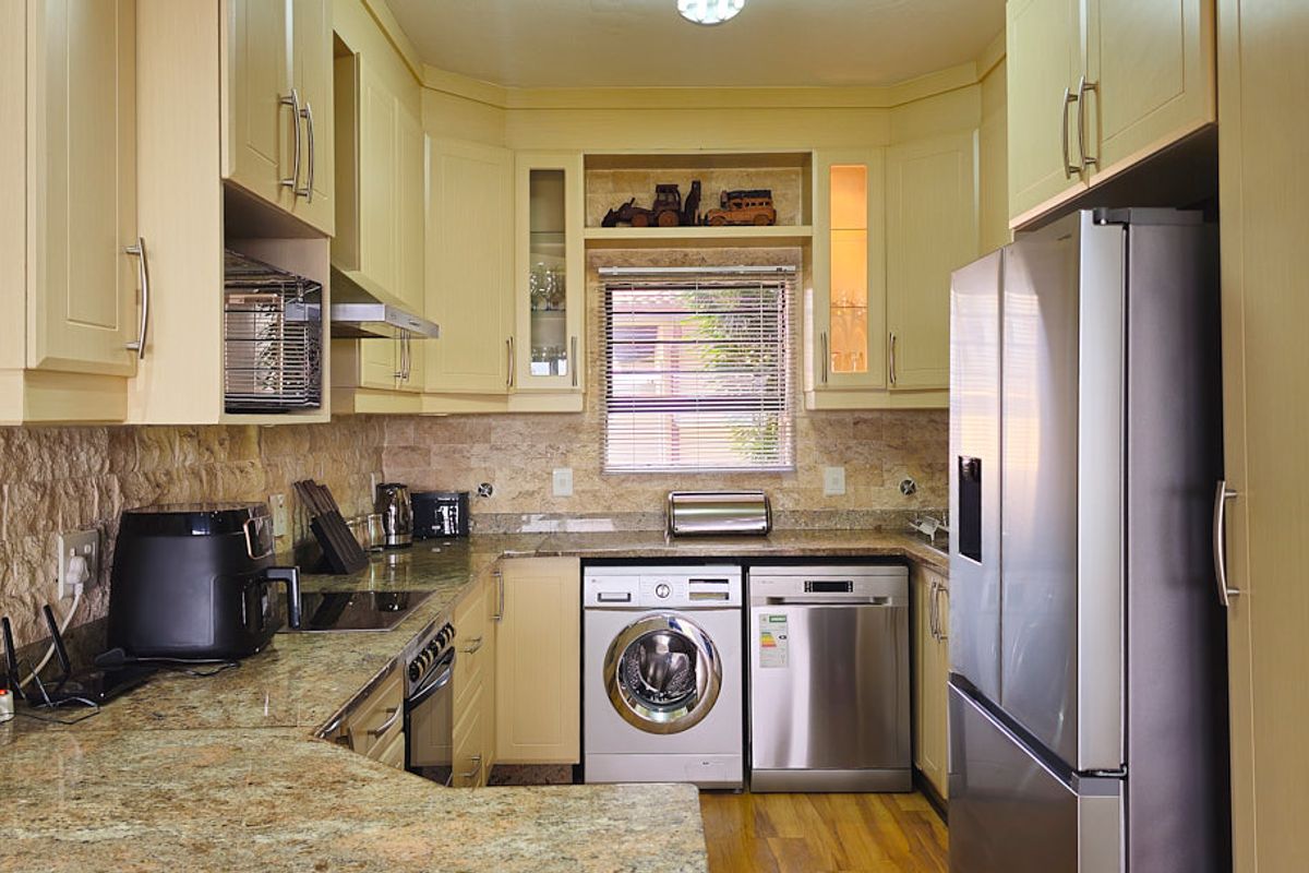 A functional kitchen featuring granite countertops, stone tile backsplash, built-in cabinetry, and integrated appliances including an oven, extractor fan, and microwave.