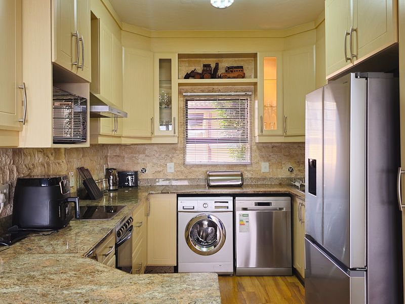 A functional kitchen featuring granite countertops, stone tile backsplash, built-in cabinetry, and integrated appliances including an oven, extractor fan, and microwave.
