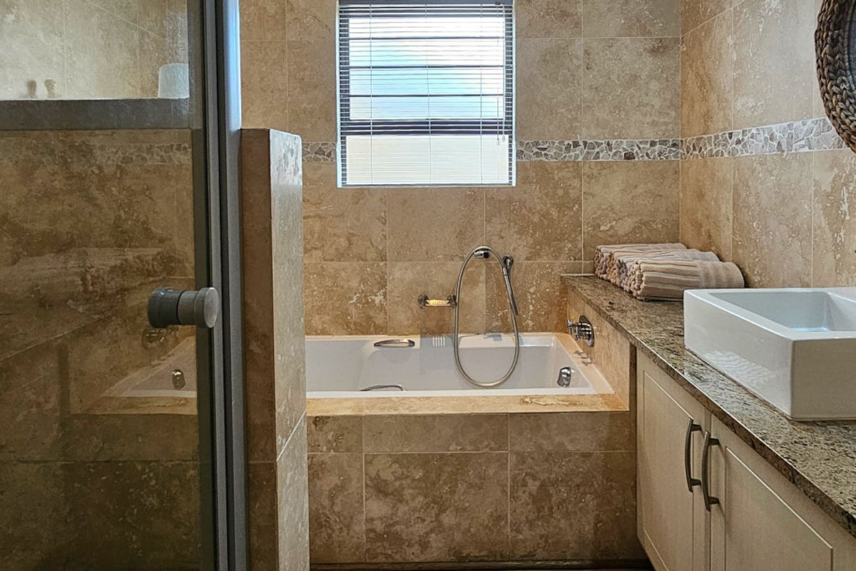 A well-maintained bathroom featuring a built-in bathtub, vessel sink with granite vanity countertop, and tiled wall finishes.