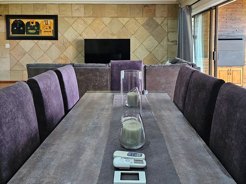 Open plan living and dining area featuring a stone tile feature wall, laminate flooring, and seamless access to an outdoor patio with a built-in braai.