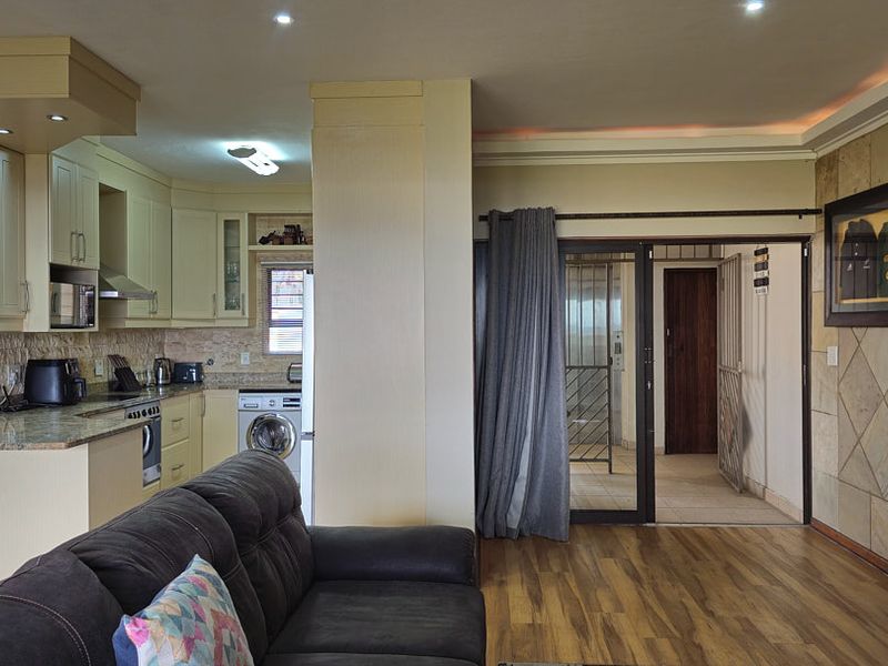 Open-plan living area featuring a modern kitchen with granite countertops, laminate flooring, and a stone feature wall, leading to a secure entrance.