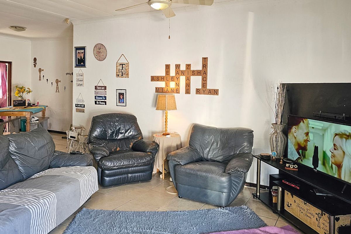 A living room area featuring tiled flooring and a ceiling fan, with an open-plan layout leading to an adjacent space.