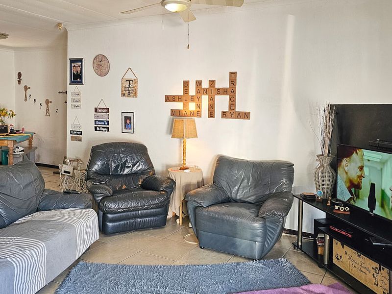 A living room area featuring tiled flooring and a ceiling fan, with an open-plan layout leading to an adjacent space.