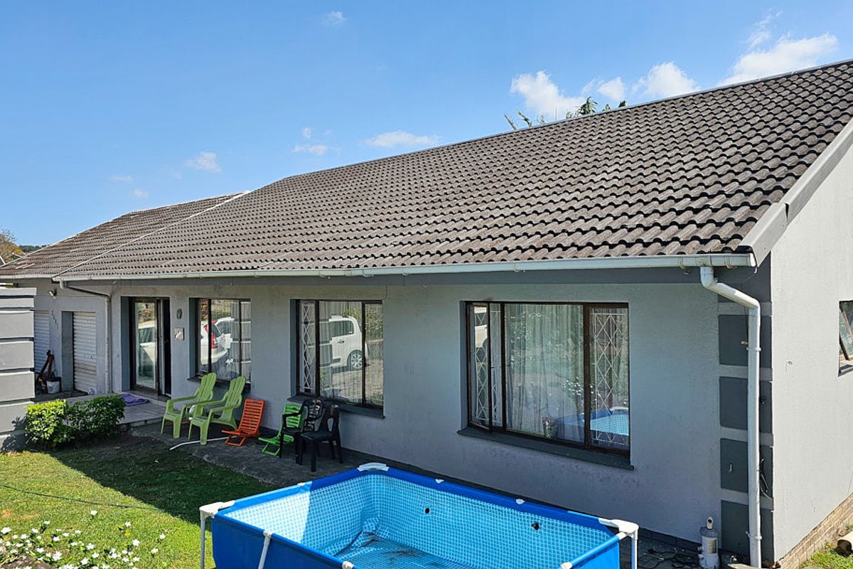 Rear view of the house featuring a concrete tile roof, aluminium window frames with security bars, and a paved patio area.