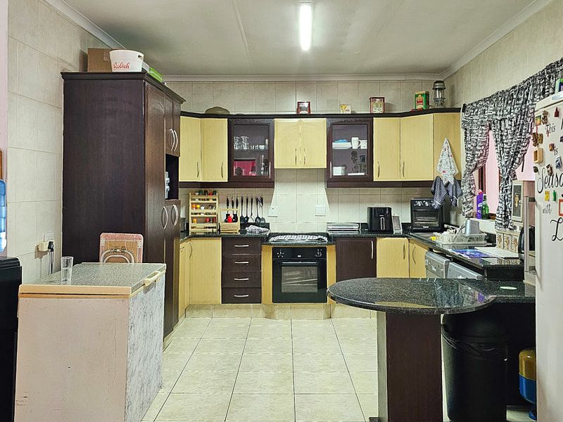 A functional kitchen featuring two-tone cabinetry, granite countertops, built-in oven and hob, and tiled flooring throughout.
