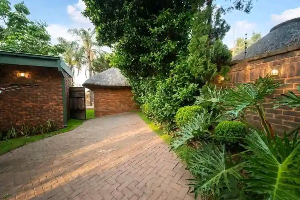 A well-maintained rear garden area featuring brick paving, established landscaping, face brick boundary walls, and a charming thatched roof structure.