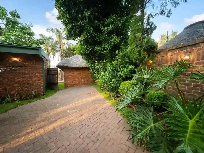 A well-maintained rear garden area featuring brick paving, established landscaping, face brick boundary walls, and a charming thatched roof structure.