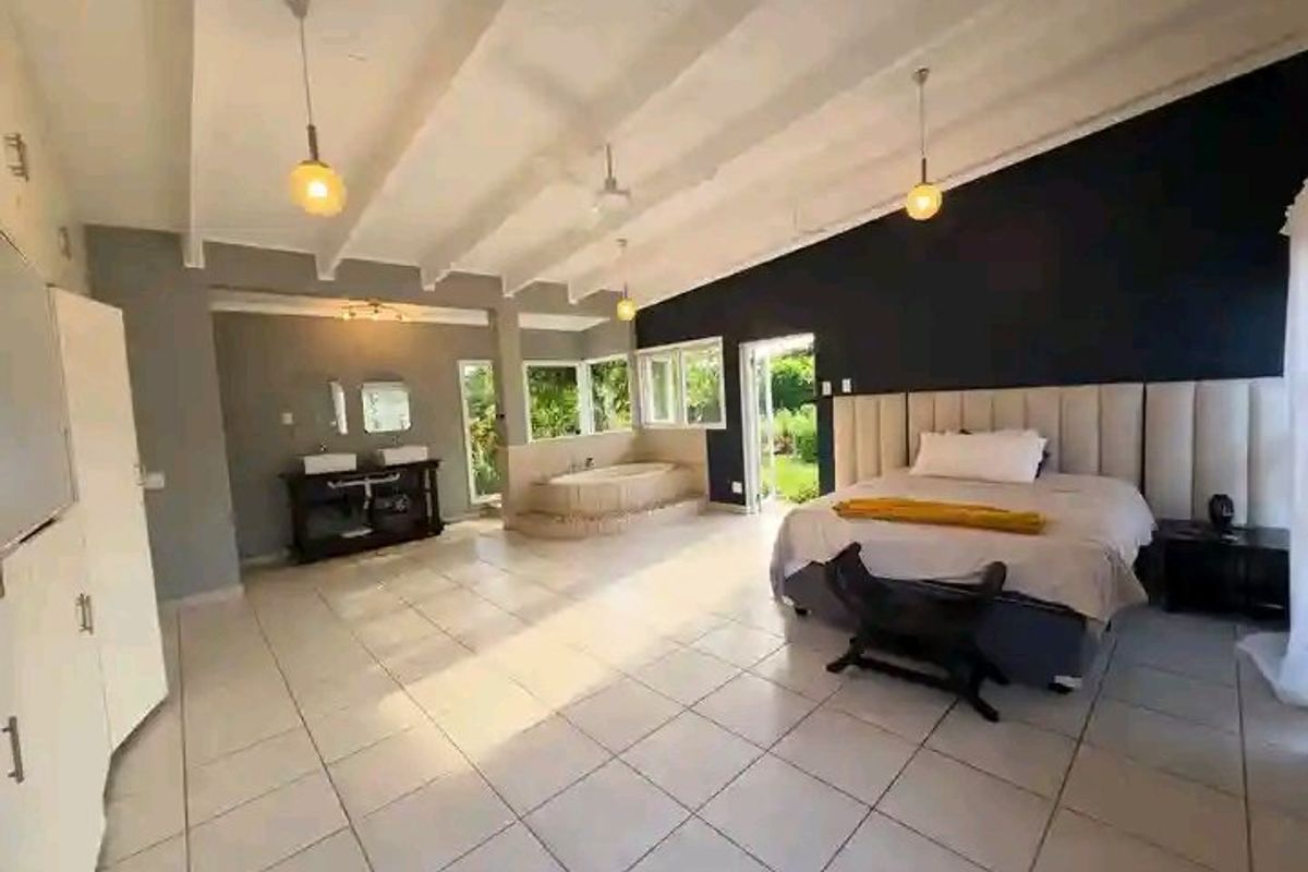 Spacious open-plan bedroom featuring an integrated en-suite bathroom with a built-in bathtub, double vanity, and exposed beam ceilings with modern pendant lighting.
