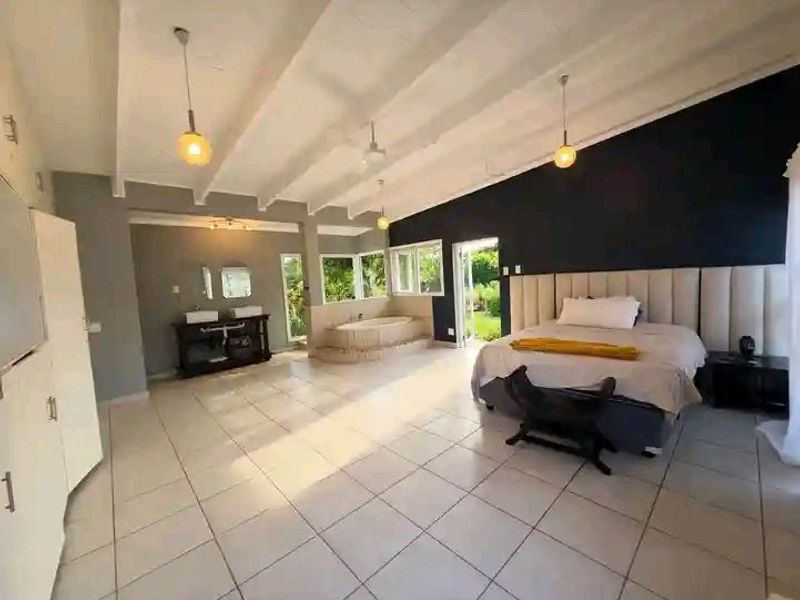 Spacious open-plan bedroom featuring an integrated en-suite bathroom with a built-in bathtub, double vanity, and exposed beam ceilings with modern pendant lighting.