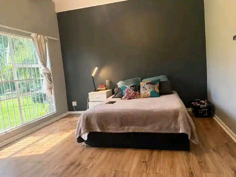 A bedroom featuring laminate flooring, a large window with security bars, and a dark accent wall.
