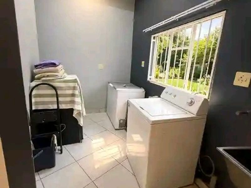 A functional laundry room featuring tiled flooring, a sink, and a window with security bars, offering a practical space for household utility tasks.
