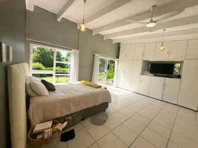 Spacious bedroom featuring tiled flooring, exposed beam ceilings, ceiling fans, and extensive built-in cabinetry with direct access to the garden through sliding doors.