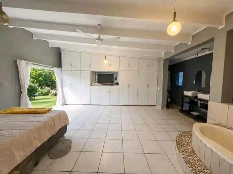 Spacious bedroom featuring extensive built-in cabinetry, tiled flooring, exposed ceiling beams, and an integrated en-suite bathroom area with a bathtub and double vanity.