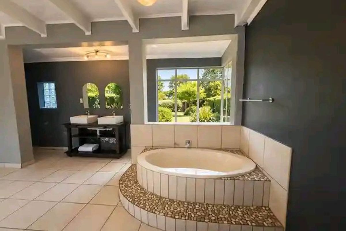 Spacious bathroom featuring a built-in circular bathtub with pebble detailing, double vanity, and large windows overlooking the garden.