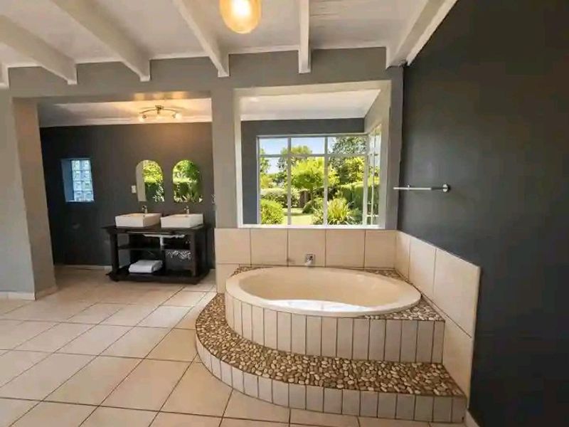 Spacious bathroom featuring a built-in circular bathtub with pebble detailing, double vanity, and large windows overlooking the garden.