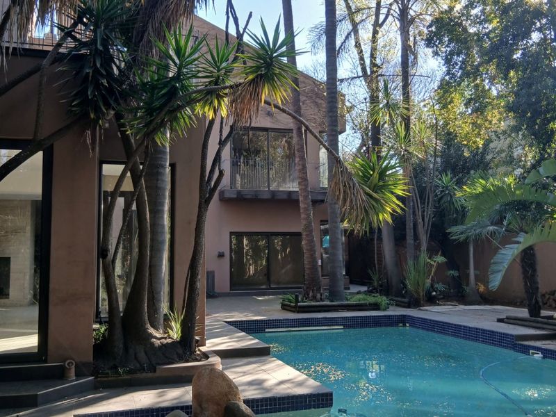 A rear exterior view featuring a swimming pool with a tiled surround, mature trees, and access to the main house via sliding glass doors.