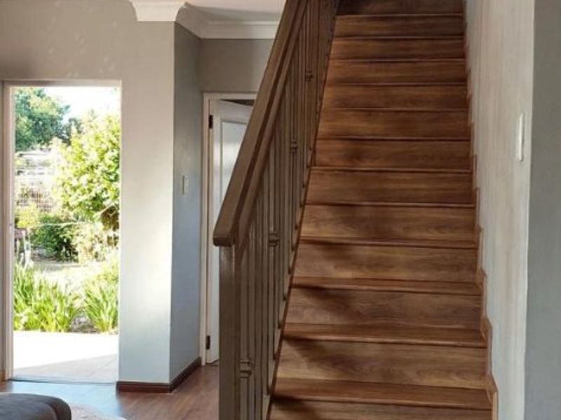 A bright hallway featuring a wooden staircase with a matching balustrade, laminate flooring, and neutral wall finishes leading to an outdoor entrance.