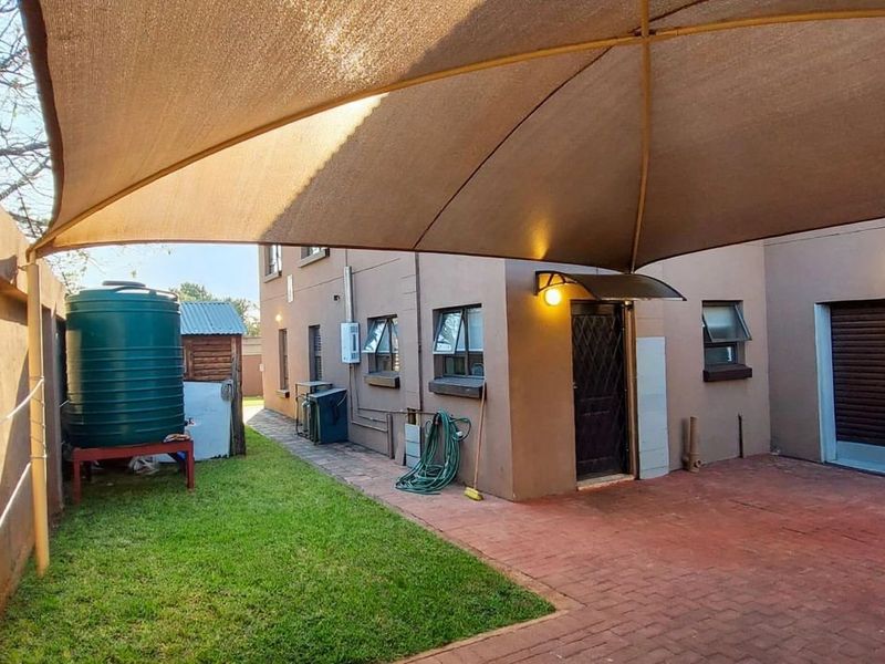 Rear exterior area featuring a paved driveway, roller garage door, shade sail covering, and a water storage tank set against a boundary wall.