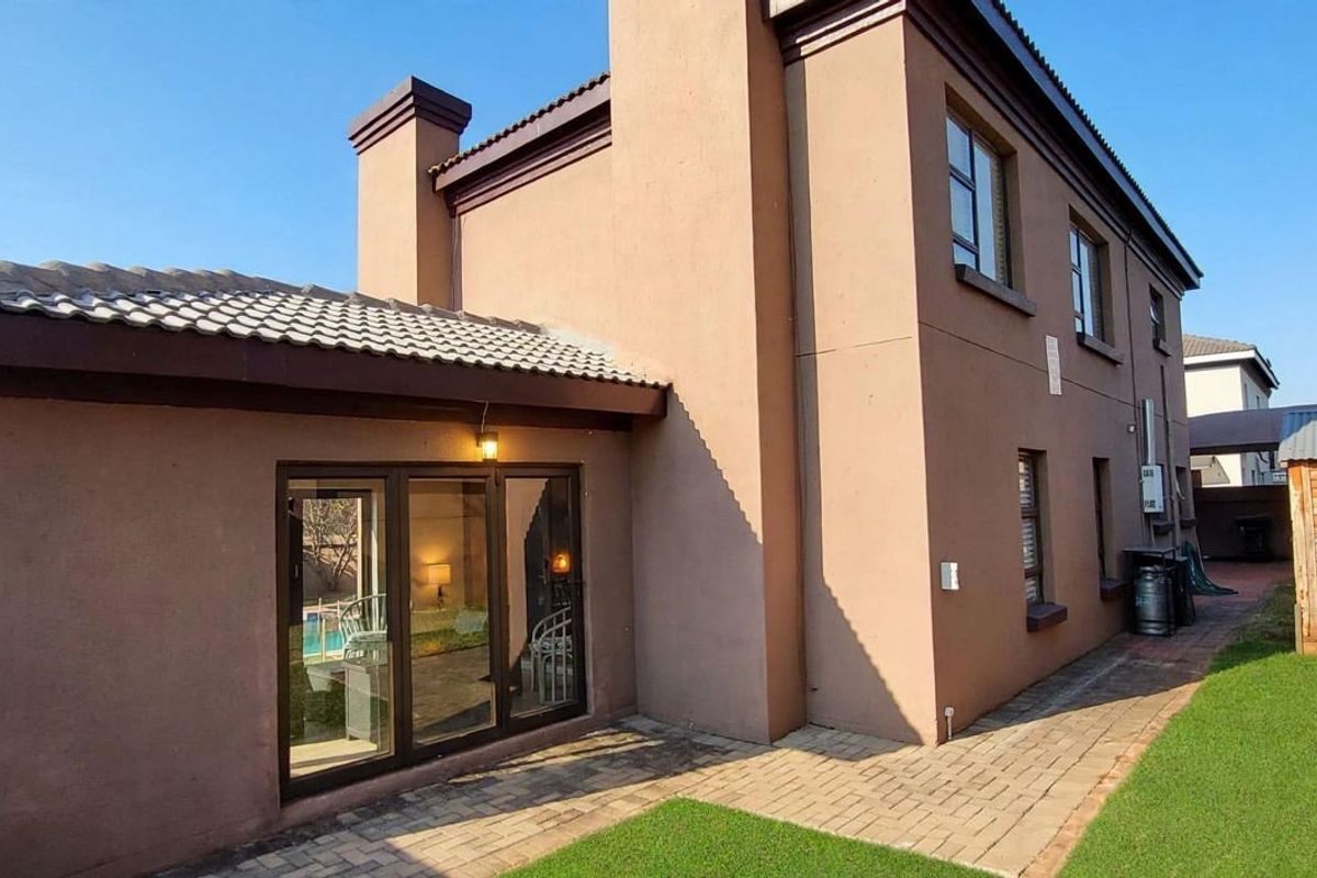 Rear view of the house featuring a paved patio area, sliding glass doors, and a well-maintained garden space.