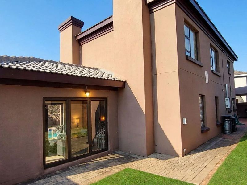 Rear view of the house featuring a paved patio area, sliding glass doors, and a well-maintained garden space.
