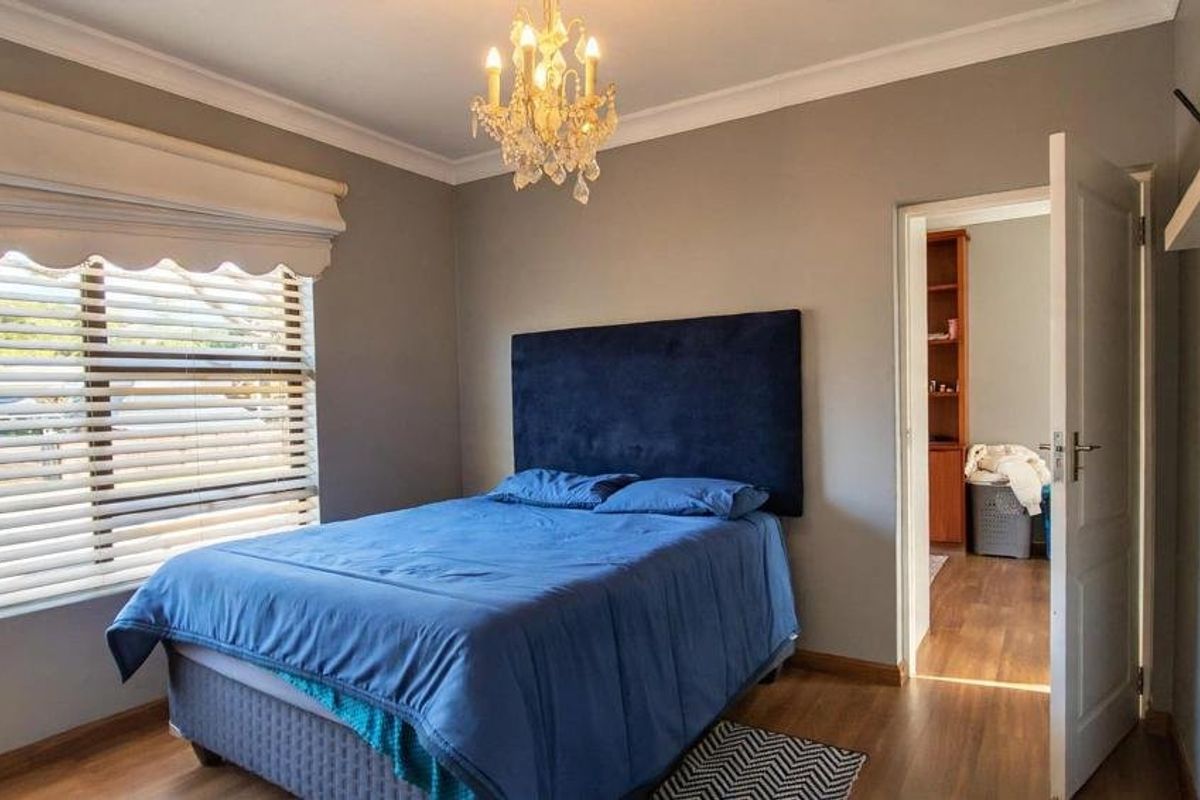 A well-maintained bedroom featuring laminate flooring, neutral wall tones, and a large window with fitted venetian blinds.