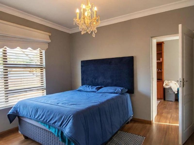 A well-maintained bedroom featuring laminate flooring, neutral wall tones, and a large window with fitted venetian blinds.