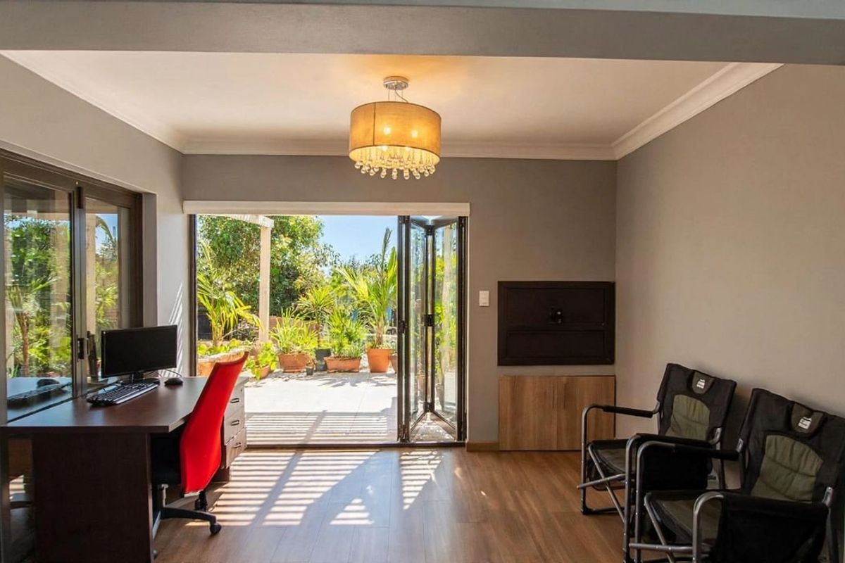 A bright living area featuring laminate flooring, modern pendant lighting, and bi-fold doors that open onto an outdoor patio space.