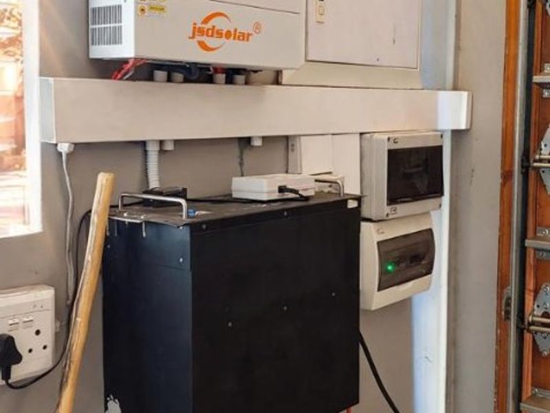 Utility area featuring a wall-mounted solar inverter and a stacked lithium battery energy storage system.