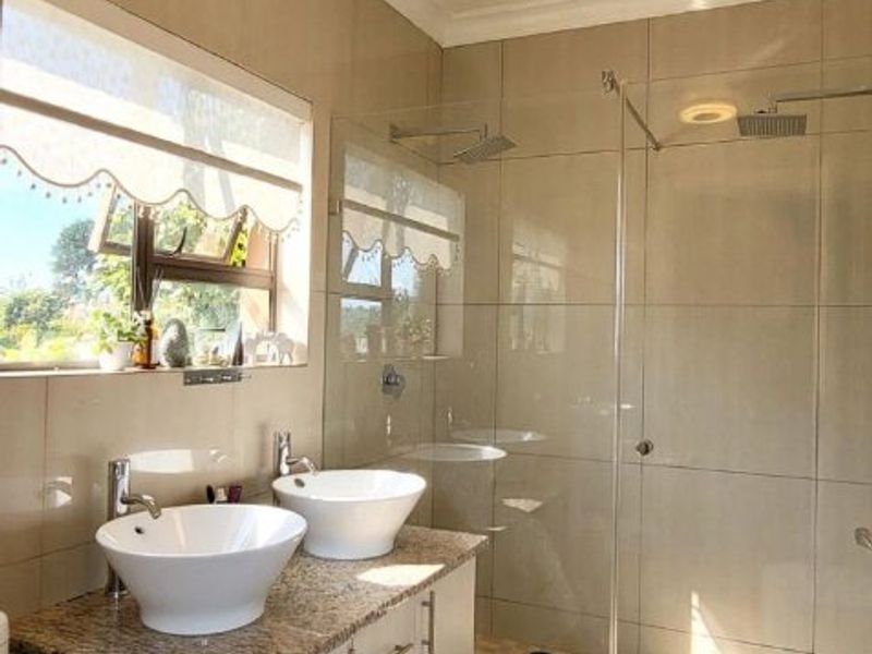 Modern bathroom featuring a double vanity with granite countertop, glass-enclosed walk-in shower with rain shower head, and neutral wall tiling.