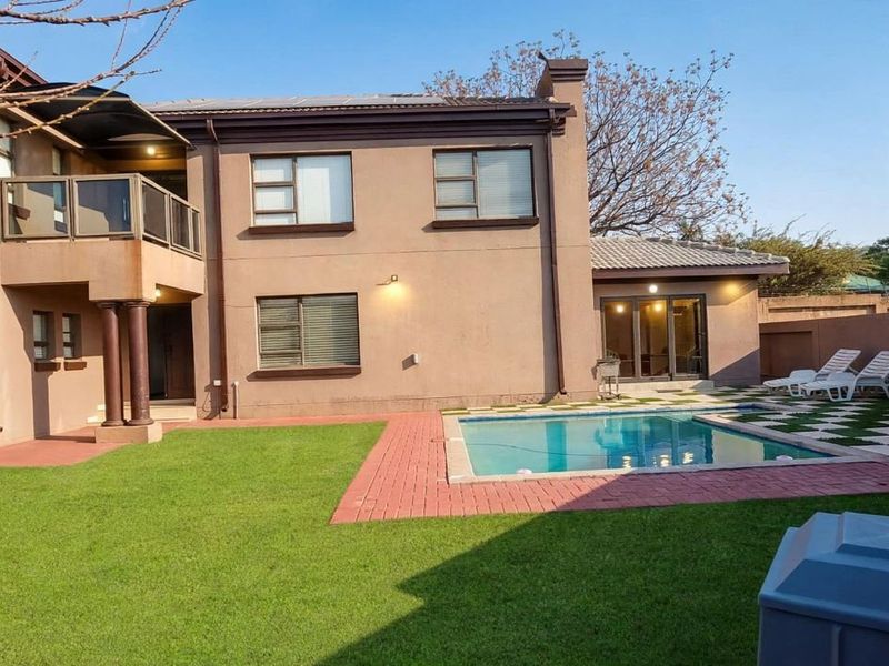Rear view of the property featuring a swimming pool, paved patio area, landscaped lawn, and a balcony overlooking the garden.