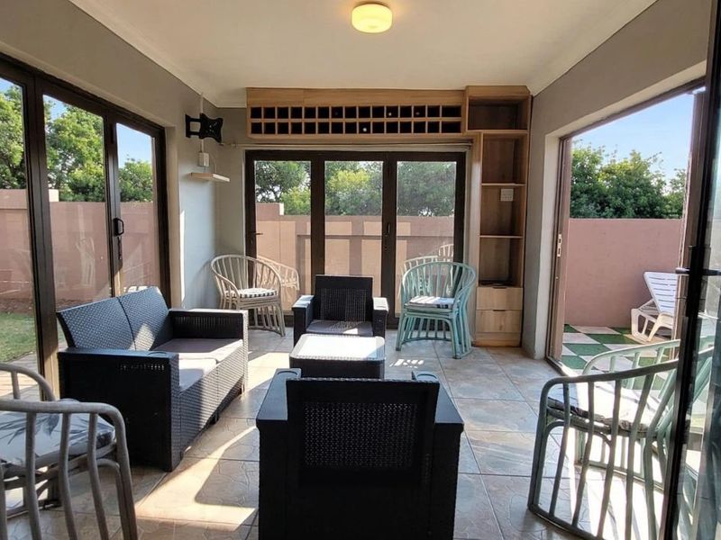 A bright, enclosed patio area featuring tiled flooring, built-in shelving, and large sliding glass doors providing access to the garden.