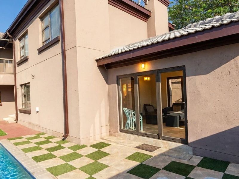 Rear view of the property featuring a swimming pool, a tiled patio area with sliding glass doors, and a balcony on the upper level.