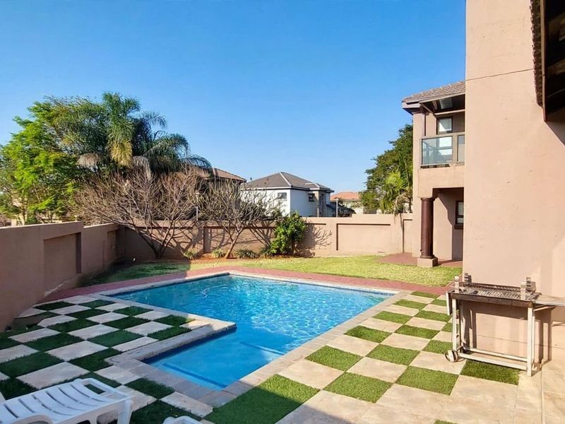 A private backyard featuring a swimming pool, paved patio area with artificial grass inlay, and direct access to the home via sliding glass doors.