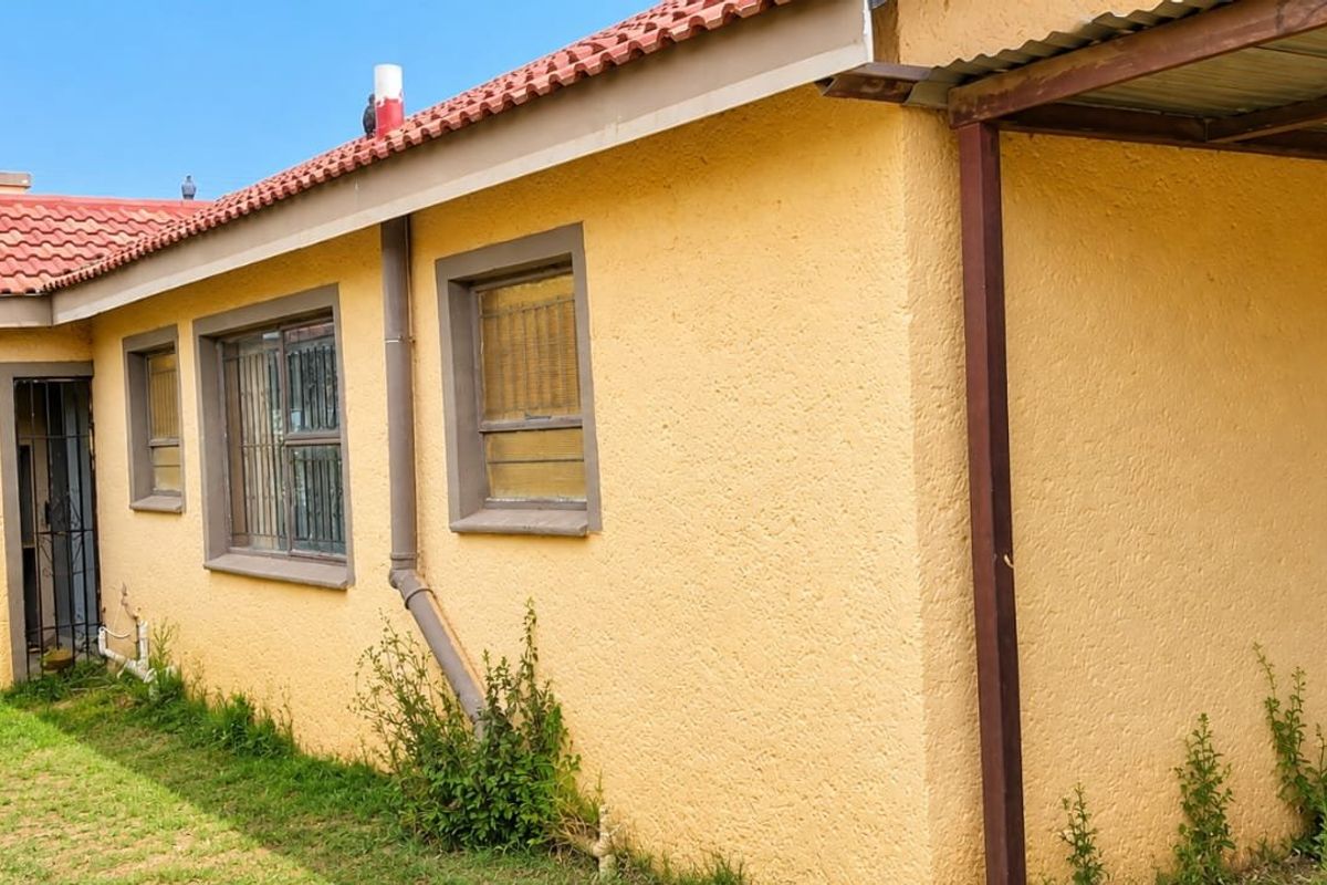 Rear exterior view of the house featuring a terracotta tiled roof, stucco walls, and a covered patio area with metal structural supports.