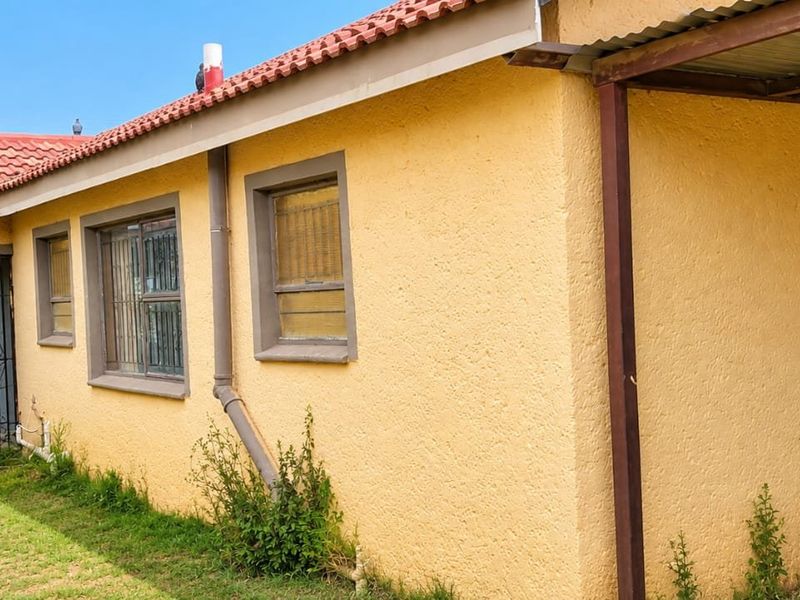 Rear exterior view of the house featuring a terracotta tiled roof, stucco walls, and a covered patio area with metal structural supports.