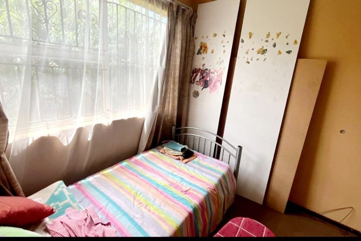 A bedroom featuring a window with security bars and plain wall finishes, requiring cosmetic updates to improve the overall condition.